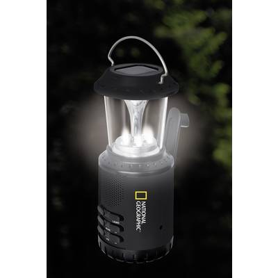 Eine schwarze Laterne mit transparentem Glas und leuchtendem Licht, versehen mit dem 'National Geographic'-Logo, vor einem unscharfen Naturhintergrund.