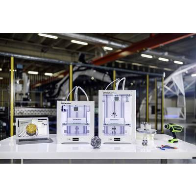 3D-Druckgeräte in einer Werkstatt. Zwei Ultimaker-Drucker und Zubehör stehen auf einem Tisch. Ein Bildschirm zeigt ein 3D-Modell.