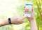 Eine Hand hält ein Smartphone mit einer Fitness-App, zeigt Balkendiagramme an. Andere Hand trägt ein Fitnessarmband, umgeben von Wald.