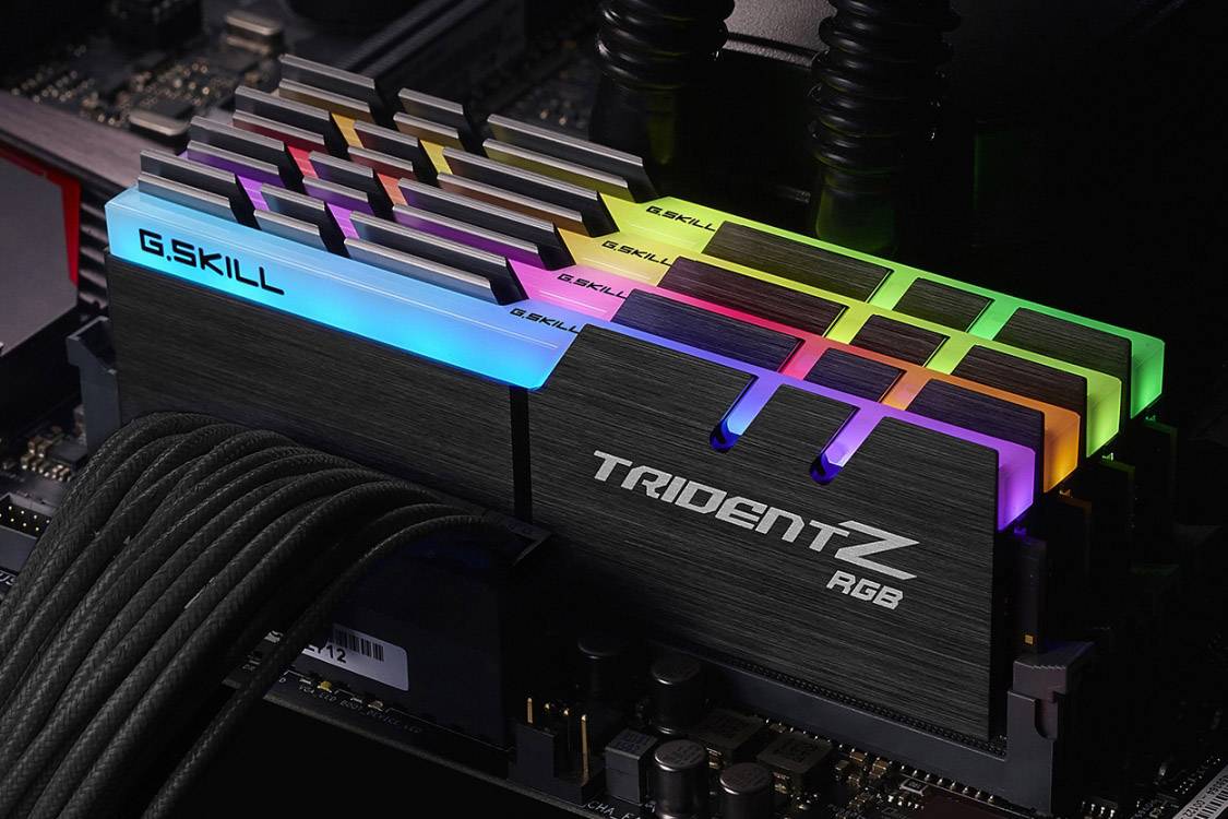 Vier G.Skill Trident Z RGB RAM-Module mit leuchtenden LEDs in verschiedenen Farben sind in einem Computer-Motherboard installiert.