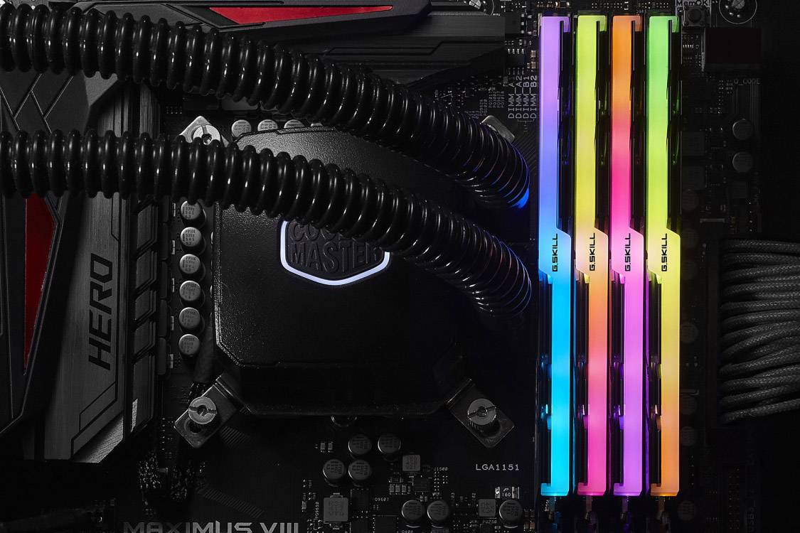 Ein Computer-Motherboard mit beleuchtetem, farbigem RGB-RAM. Vier RAM-Riegel leuchten in verschiedenen Farben.