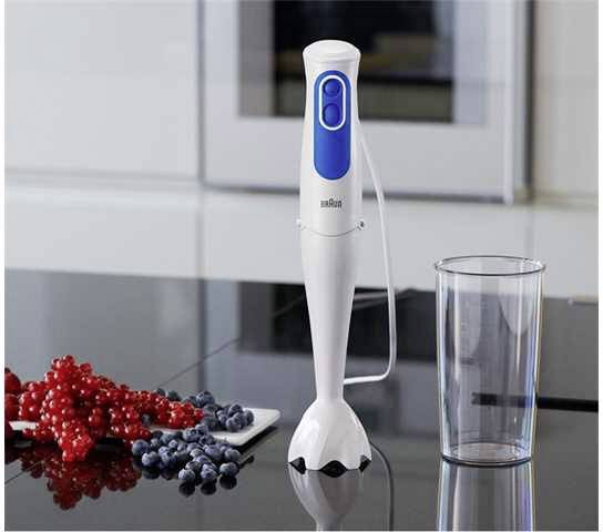 Ein weißer Stabmixer mit blauem Griff steht auf einer Küchenarbeitsplatte neben einem leeren Plastikbecher und frischen Beeren.