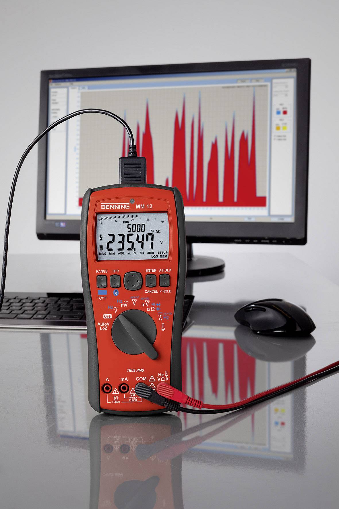 Ein Multimeter misst eine Spannung von 23,447 V auf einem Tisch vor einem Computerbildschirm, der ein grafisches Diagramm zeigt.