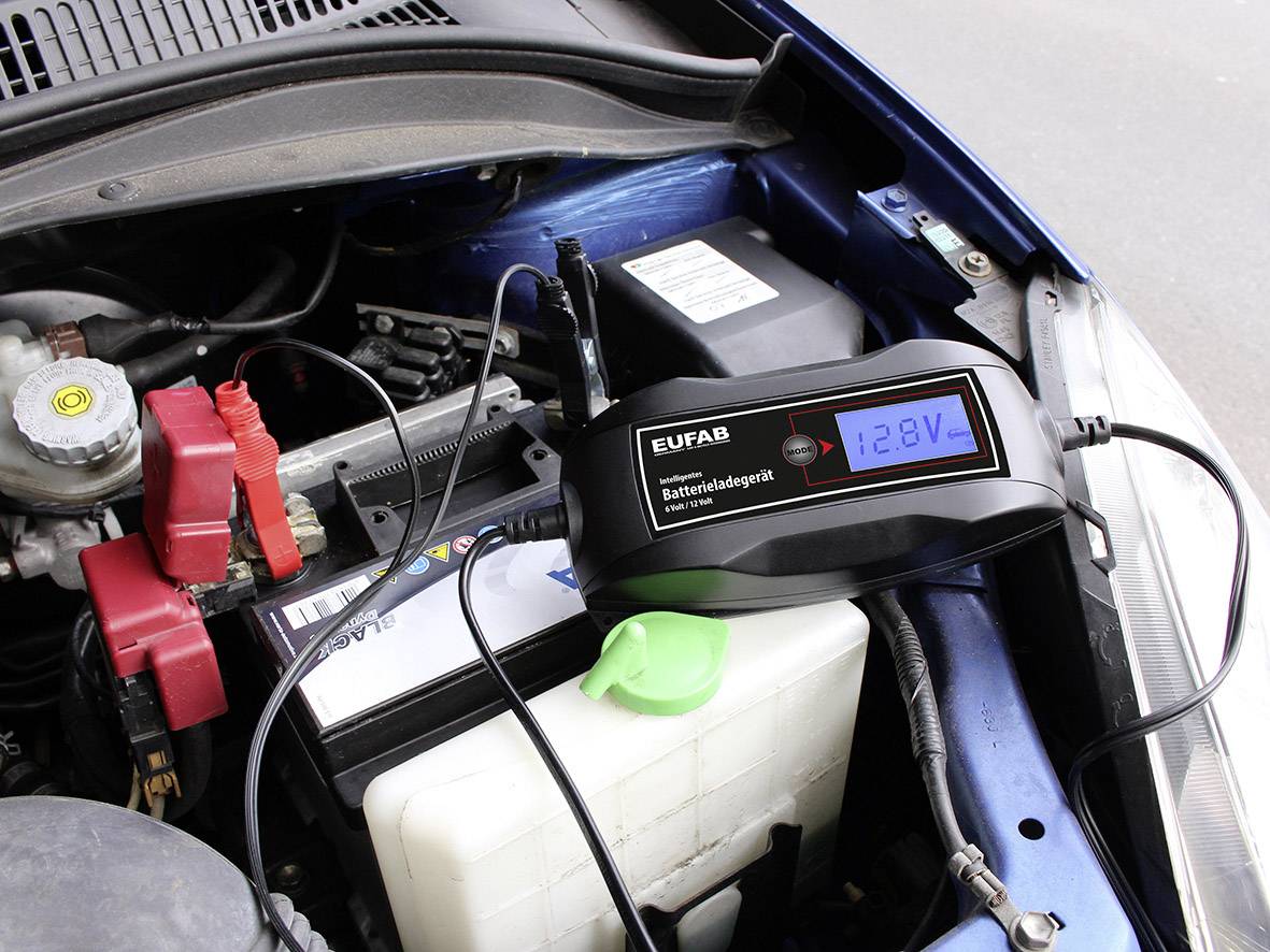 'Ein Autobatterieladegerät von EUFAB ist an eine Autobatterie angeschlossen und zeigt eine Spannung von 12,8V auf dem Display an.'