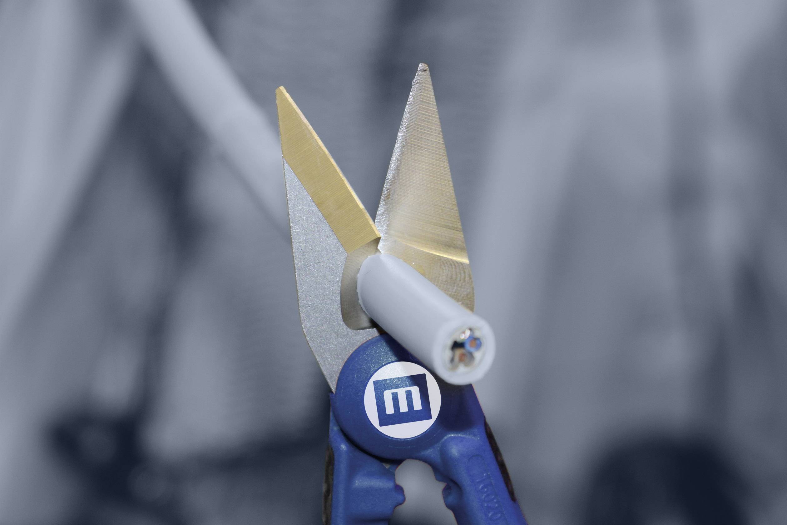 Eine blaue Abisolierzange entfernt die Isolierung von einem weißen Kabel. Im Hintergrund unscharfe Laborgeräte.