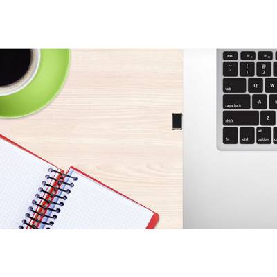 Auf einem Holztisch liegen ein aufgeschlagenes, kariertes Notizbuch und eine Tasse Kaffee. Rechts oben ist ein Teil einer Laptop-Tastatur zu sehen.
