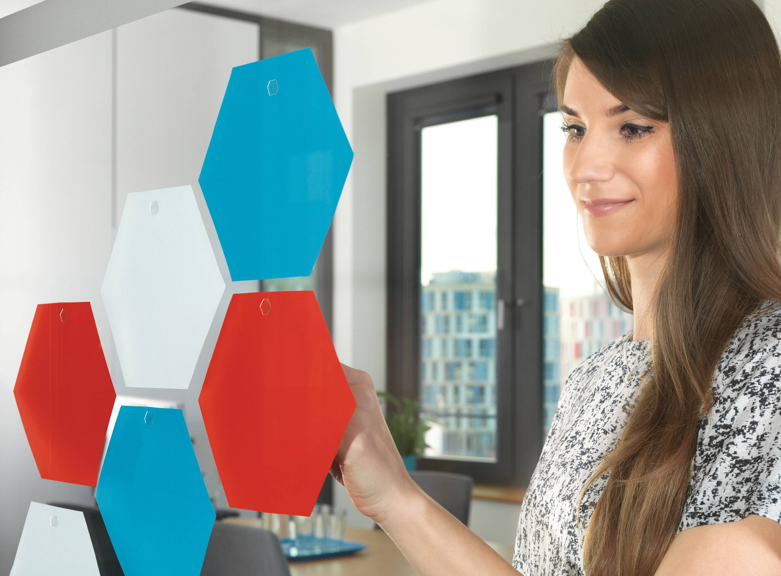Eine Frau interagiert mit bunten sechseckigen Platten in einem modernen Büro. Sie scheint konzentriert und beschäftigt zu sein.
