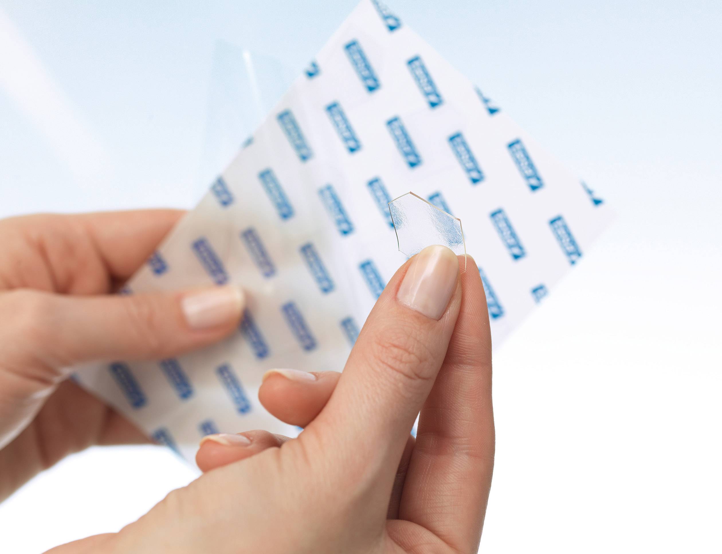 Zwei Hände halten eine transparente, sechseckige Folie und eine größere perforierte Schutzfolie in der anderen Hand.
