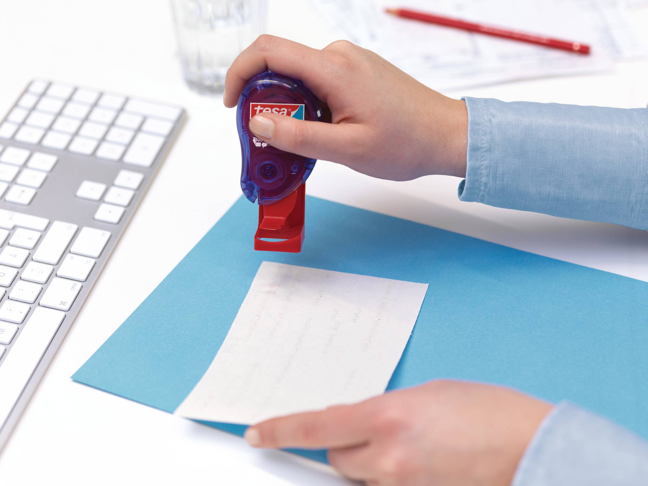Eine Person verwendet einen roten Stempel auf einem Blatt Papier auf einem blauen Ordner. Eine Computertastatur ist sichtbar.