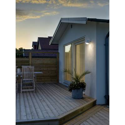 Eine Holzterrasse bei Sonnenuntergang mit Gartenmöbeln und Pflanzen. Im Hintergrund steht ein modernes Wohnhaus.