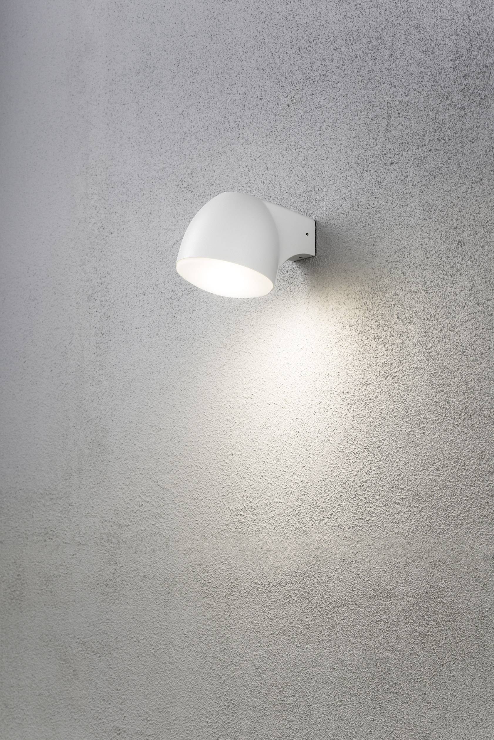 Eine einzelne weiße Wandleuchte strahlt Licht auf eine graue Wand. Sie erzeugt einen weichen Lichtschein nach unten.