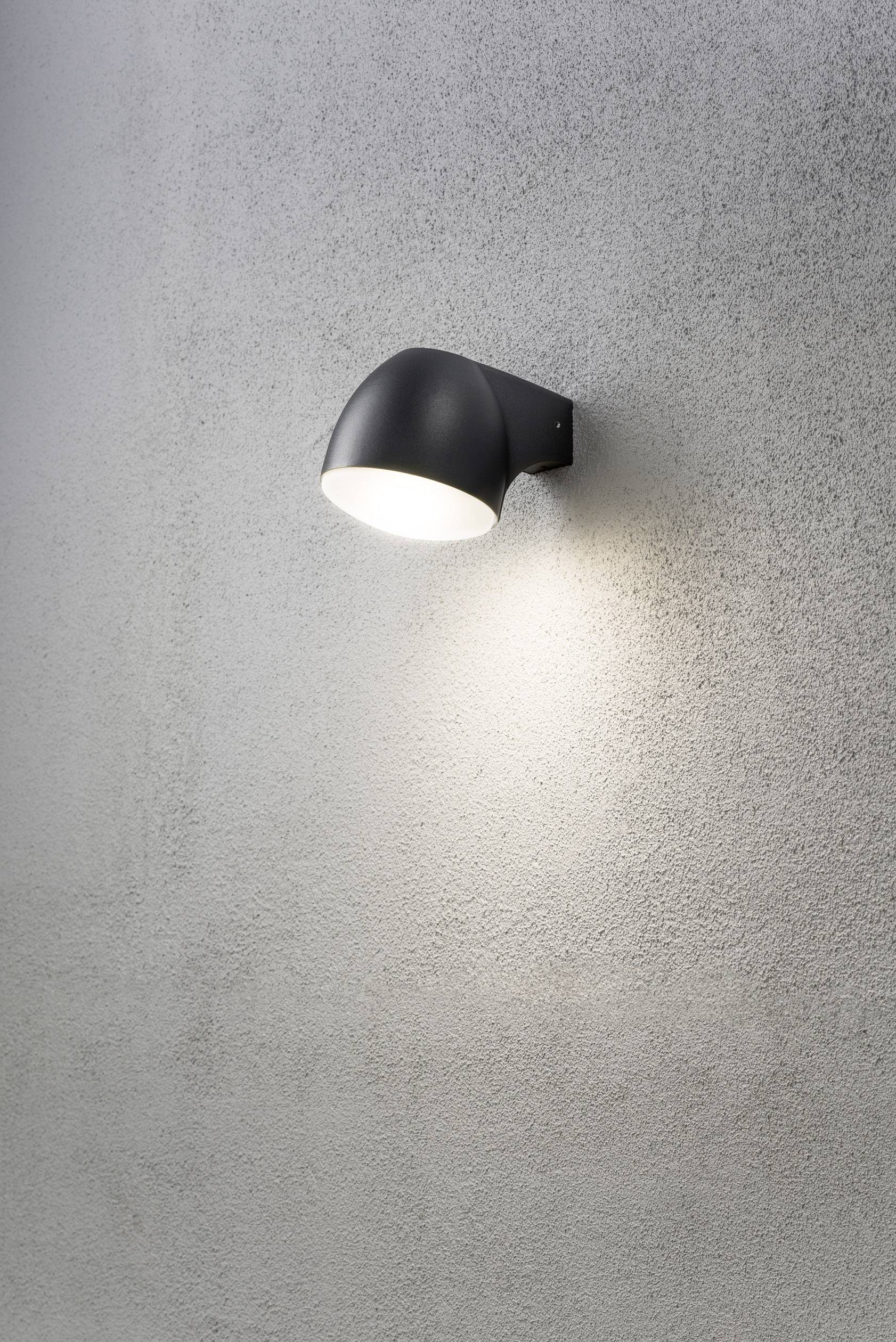 Schwarze Wandleuchte an einer grauen Wand, die helles Licht nach unten strahlt.