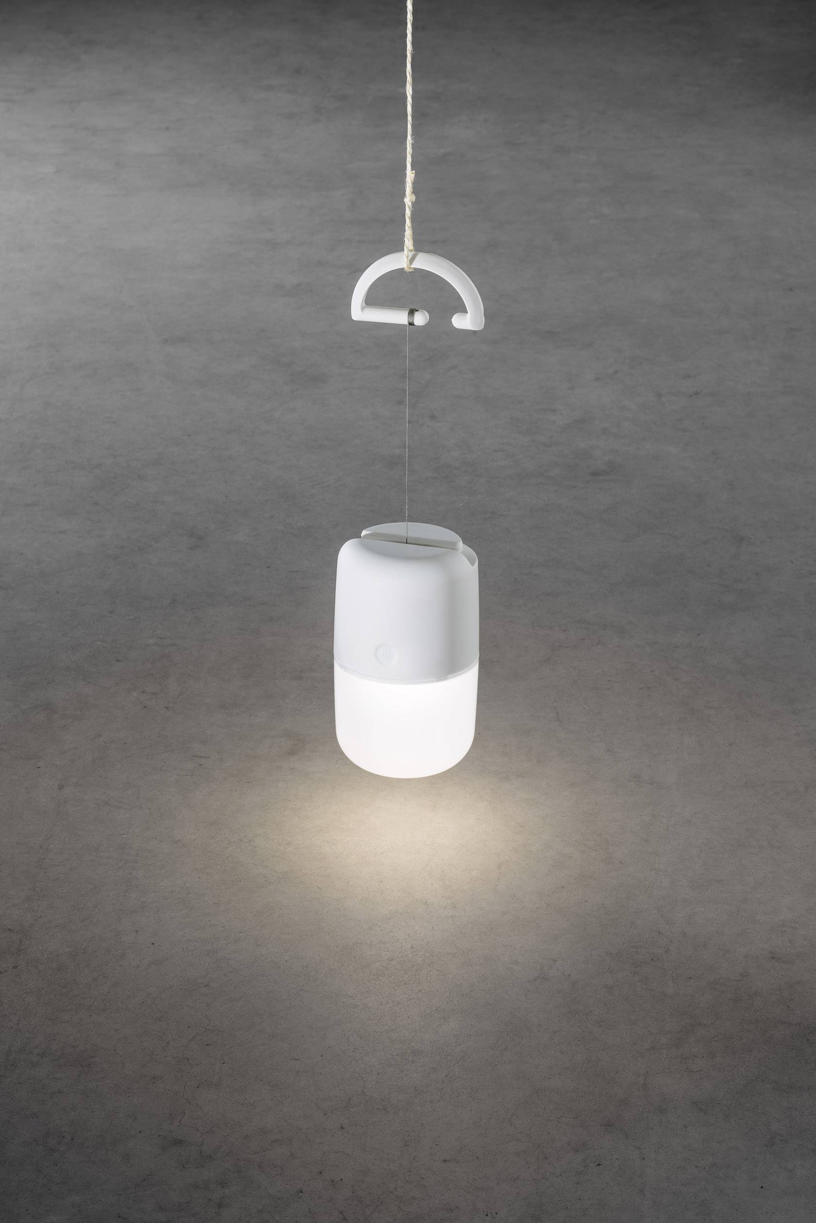 Hängende, stilvolle weiße Lampe, leuchtet sanft von oben. Beleuchtet einen grauen Boden darunter. Minimalistisches Design.