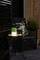 Ein gemütlich beleuchteter Balkon mit einem Rattan-Sessel und Tisch. Auf dem Tisch steht eine leuchtende Lampe, neben einem Kissen.
