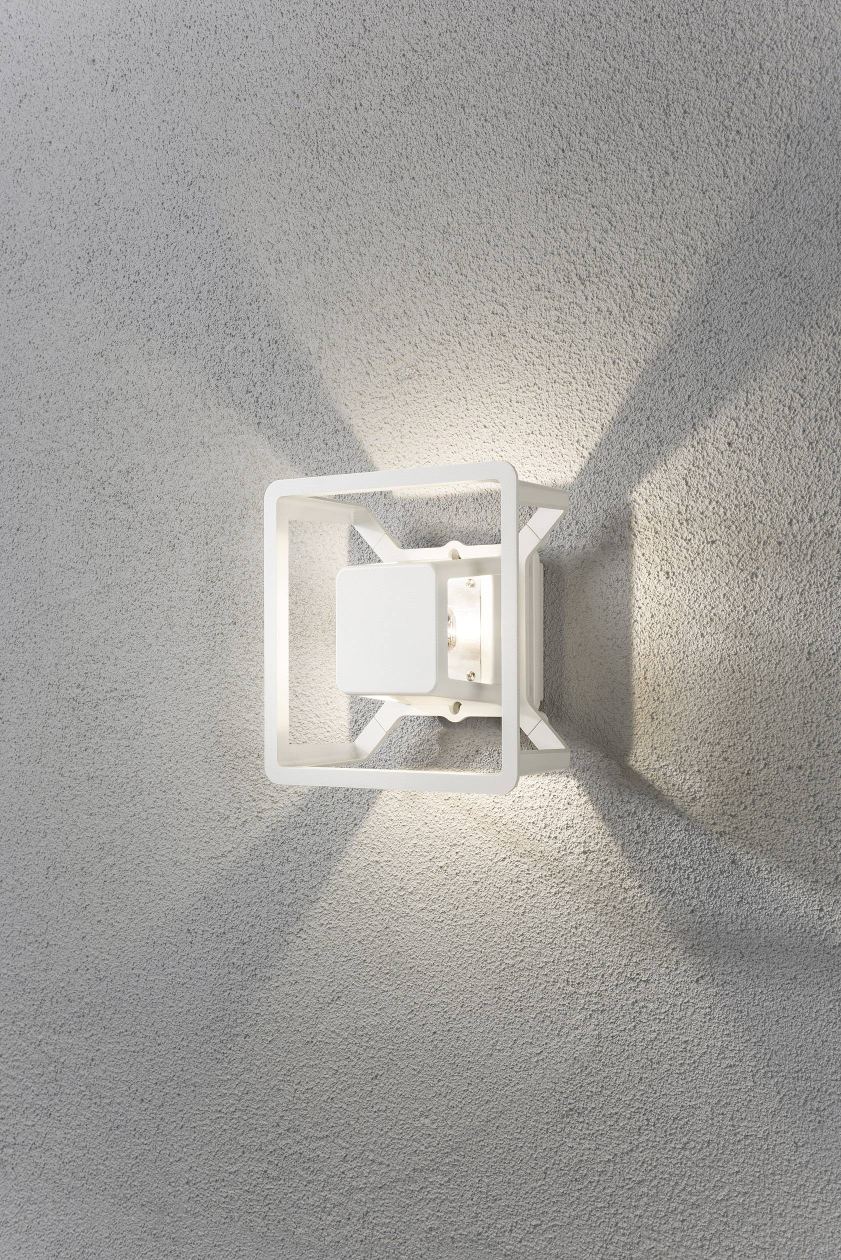Weiße Wandleuchte wirft komplexes Lichtmuster auf graue Wand. Quadratisches Design mit symmetrischem Lichtschein betont moderne Ästhetik.
