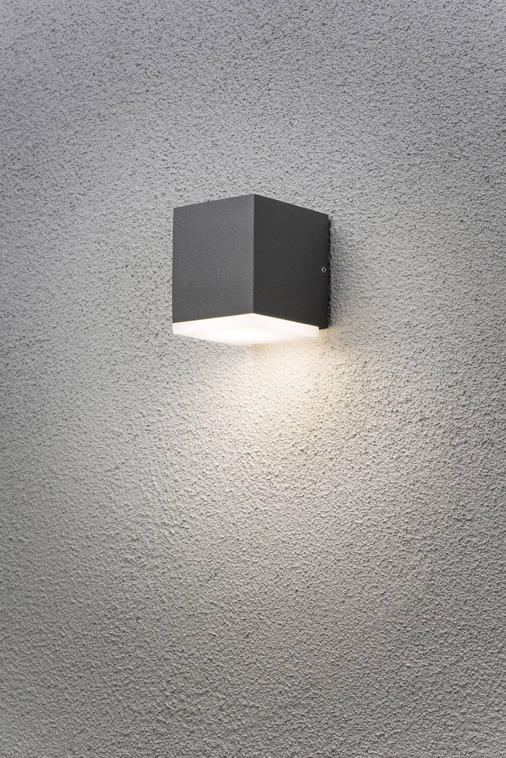 Schwarze Wandleuchte mit quadratischem Gehäuse wirft Licht auf graue strukturierte Wand.