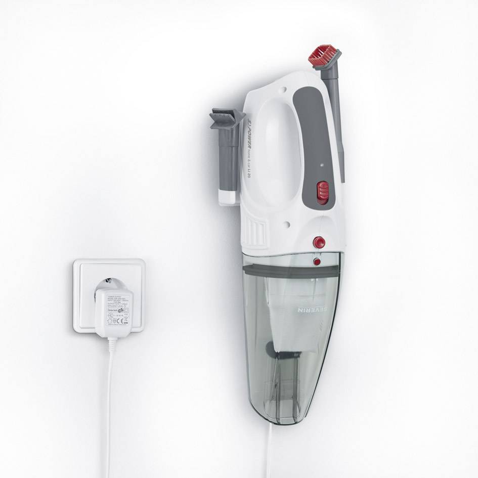 Ein an der Wand montierter, kabelloser Handstaubsauger in Weiß und Grau mit rotem Schalter, daneben eine Steckdose mit Netzteil.