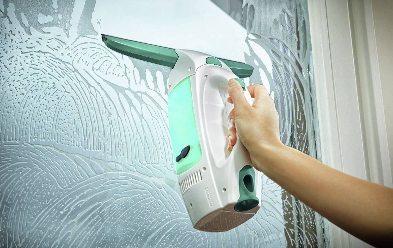 Eine Person reinigt ein Fenster mit einem elektrischen Fensterreiniger. Die Oberfläche zeigt Seifenreste, die von der Maschine entfernt werden.