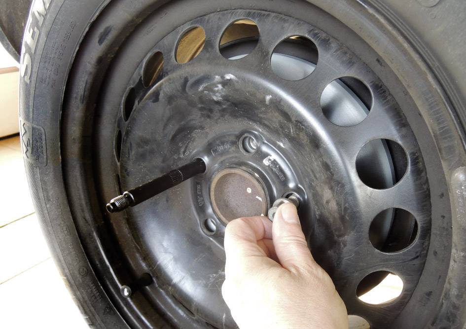 Eine Person zieht die Radmutter an einem Autoreifen an. Der Reifen ist schwarz und hat einen Ventilstift sichtbar.