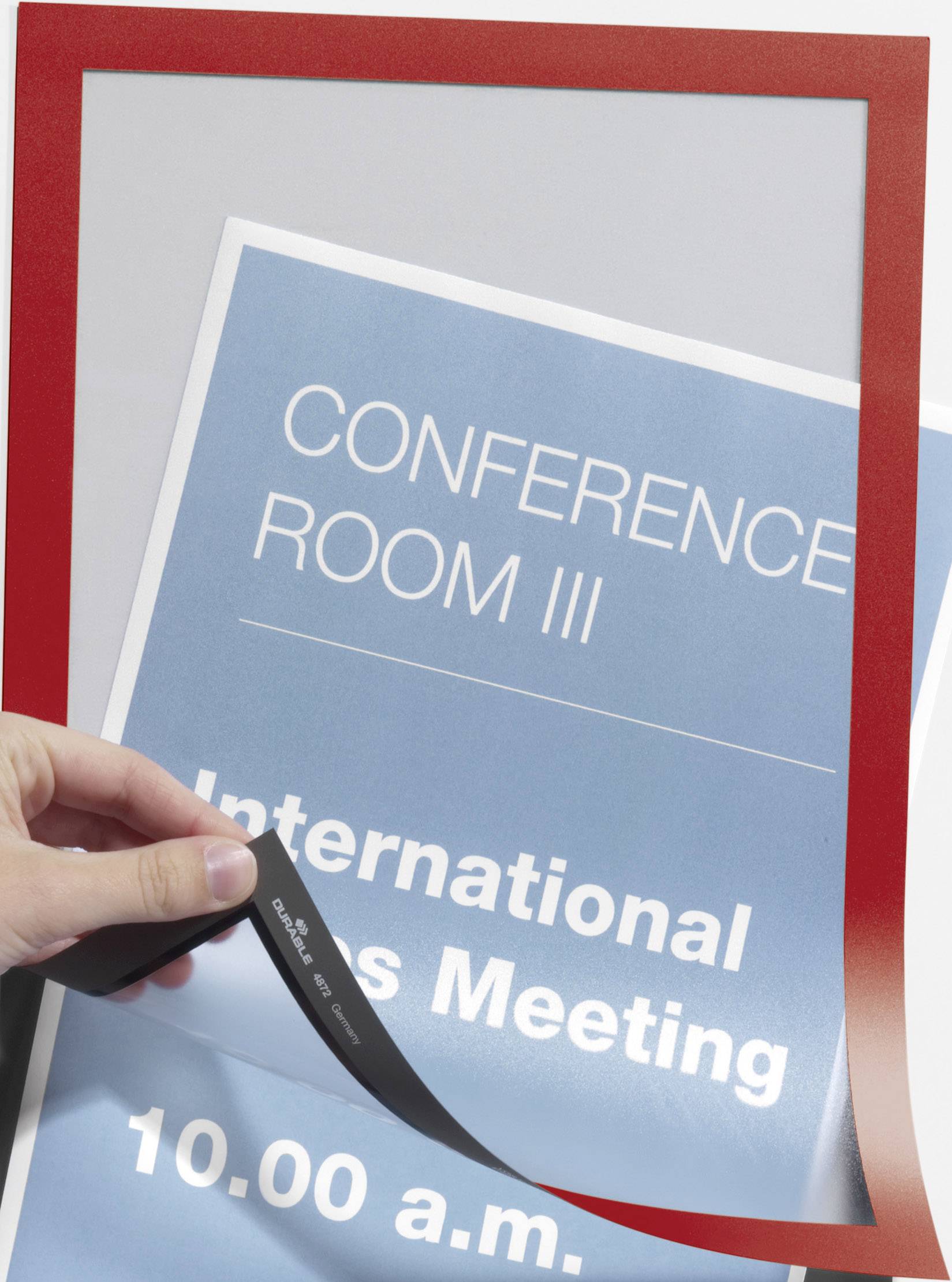 Eine Hand hält einen Ersatzrahmen über ein Schild mit der Aufschrift 'CONFERENCE ROOM III International Sales Meeting 10.00 a.m.'.