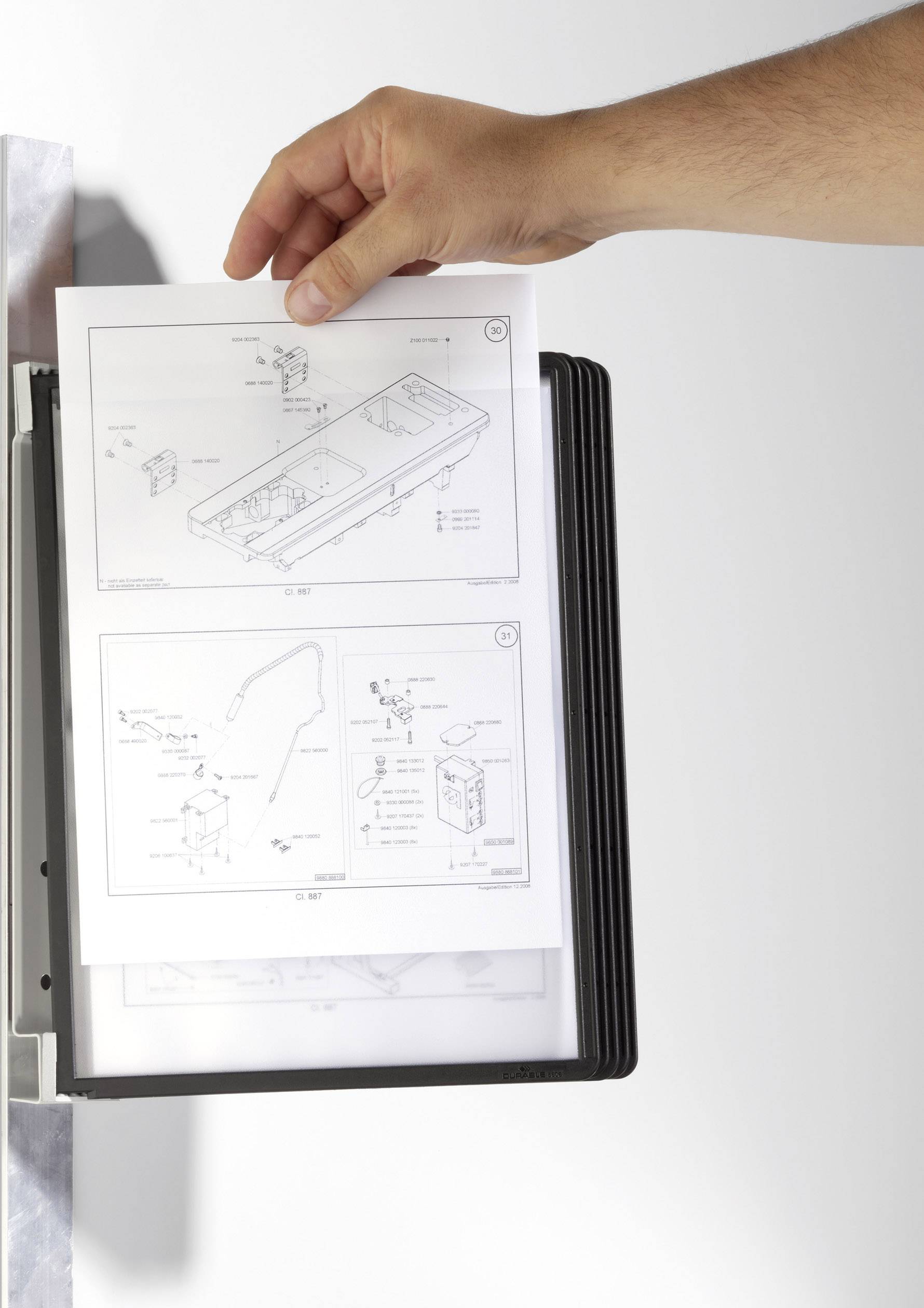 Eine Hand hält ein aufgeschlagenes technisches Handbuch mit schwarz-weißen Illustrationen und Anweisungen.