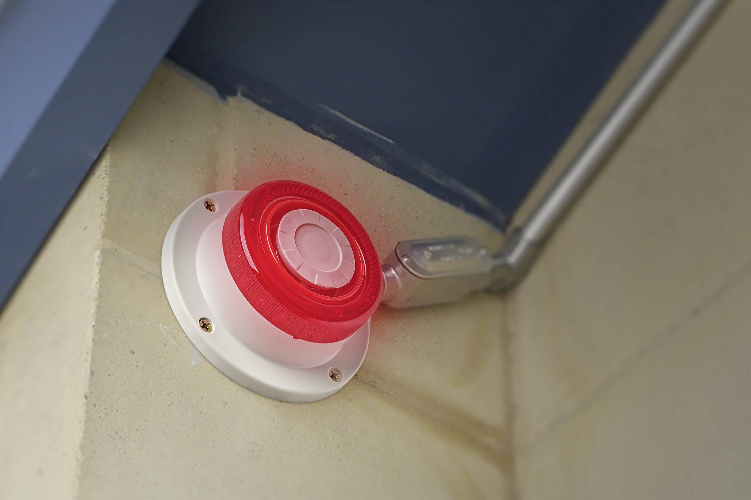 Ein roter Alarmknopf leuchtet in einer Ecke eines Raums, bereit für den Einsatz in einem Notfall.