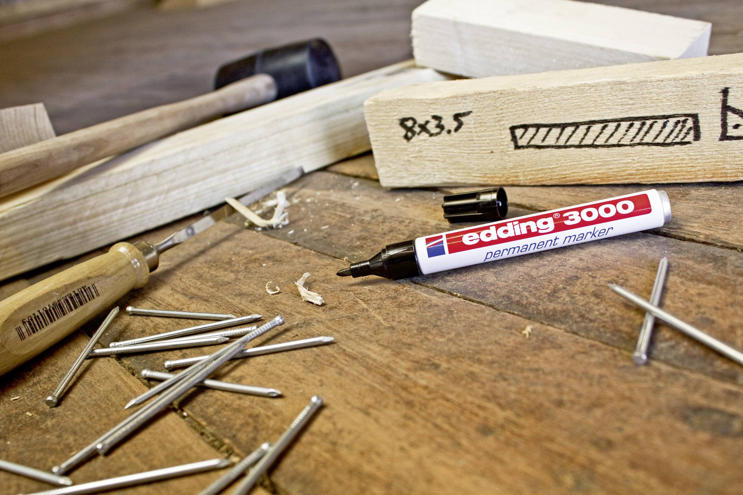 Holzstück mit einer Markierung '8x3,5', Nägel, Schraubenzieher und Edding 3000 Marker auf Holzboden, Hinweis auf handwerkliche Arbeit.