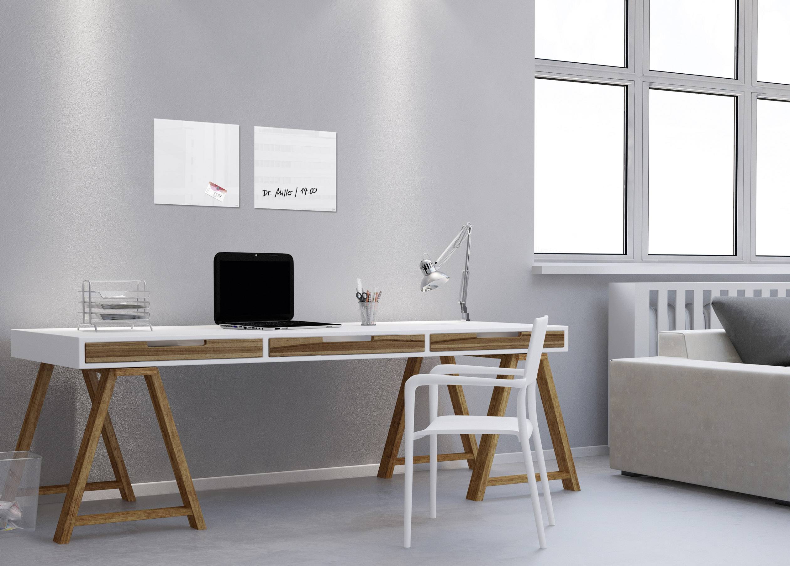 Moderner Schreibtisch mit Laptop, Lampe und Stuhl, daneben ein Sofa. Helle Wände und große Fenster lassen viel Tageslicht herein.