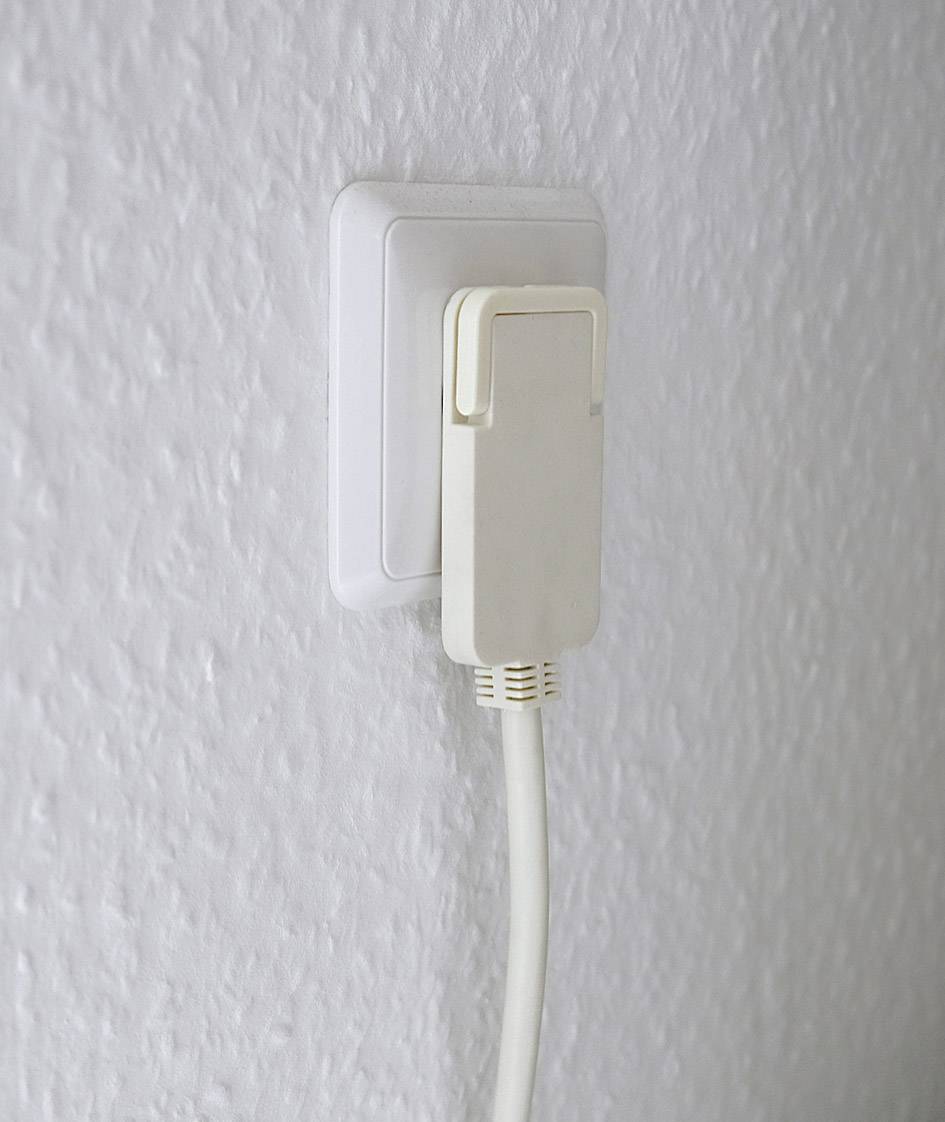 Ein weißes Flachkabel ist in eine weiße Steckdose an einer strukturierten Wand eingesteckt.