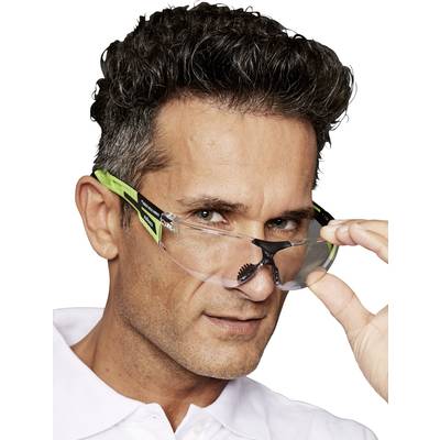 Ein Mann mit lockigem Haar trägt eine schicke Schutzbrille mit grünem Rahmen und hebt sie leicht an, während er in die Kamera blickt.