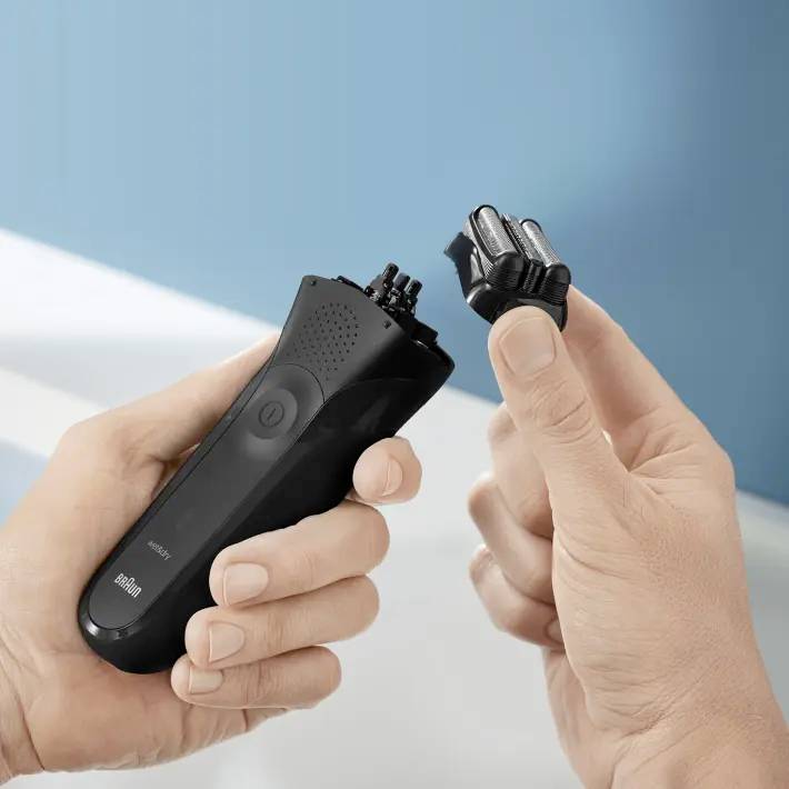 Eine Person hält einen elektrischen Rasierer mit abgenommenem Scherkopf in der Hand. Der Hintergrund ist unscharf in Blautönen.