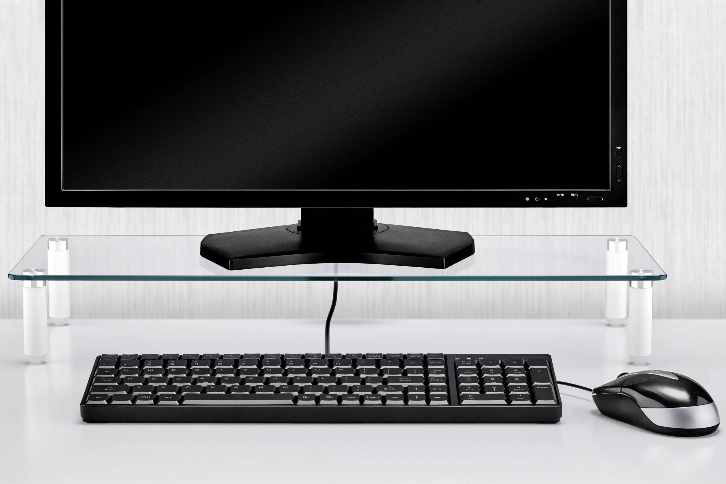 Ein Computerbildschirm steht auf einem Glasregal, darunter befinden sich eine Tastatur und eine Maus auf einem weißen Schreibtisch.