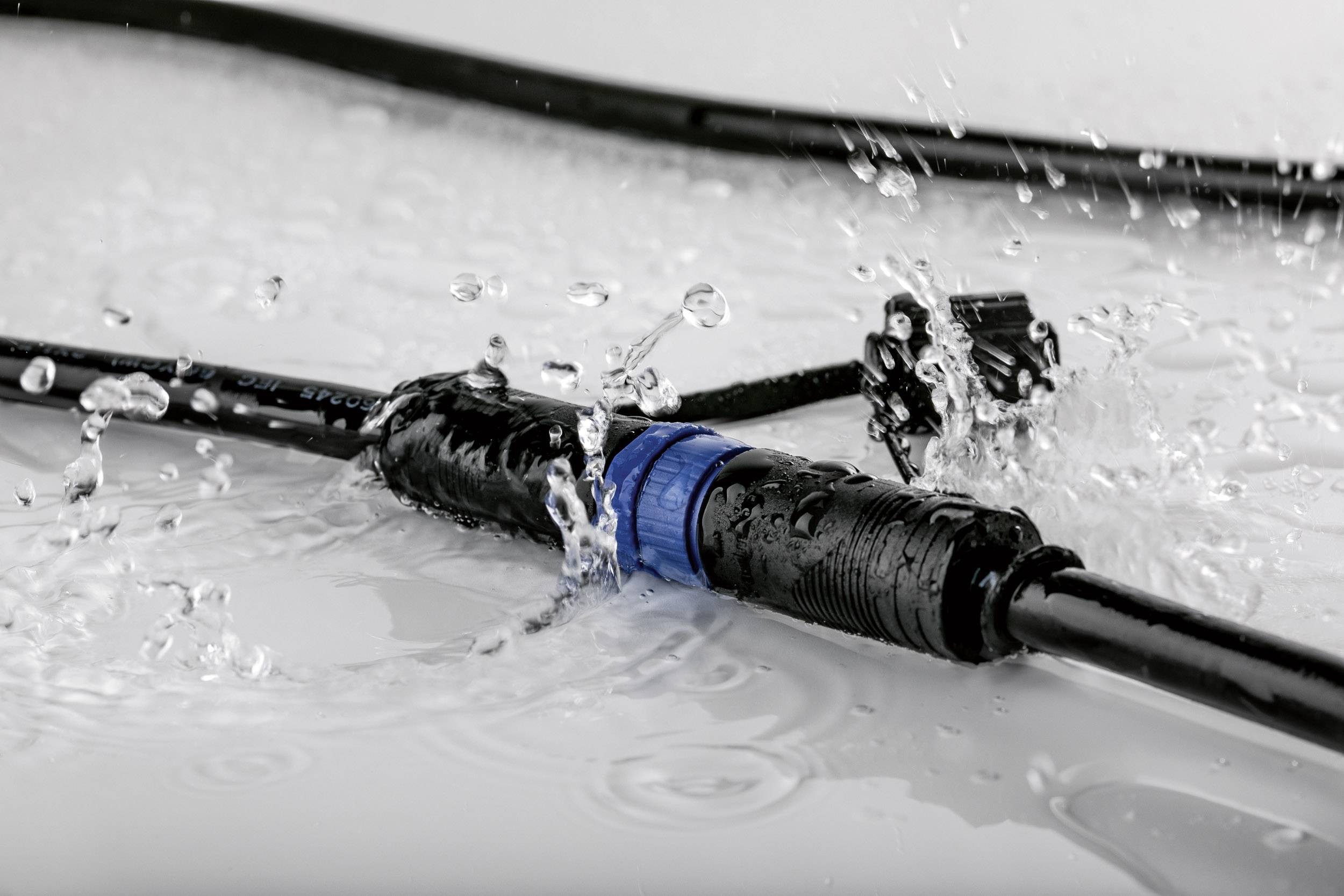 Ein wasserdichter Kabelverbinder mit blauer Dichtung liegt auf einer nassen Oberfläche, während Wasser darüber spritzt.