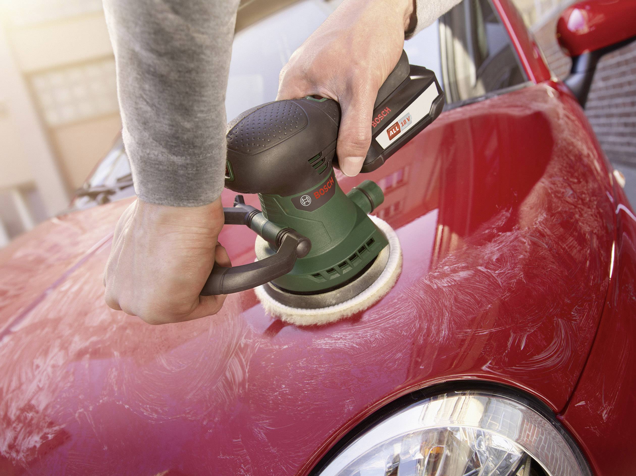 Person poliert mit einer Bosch-Autopoliermaschine die rote Motorhaube eines Autos.