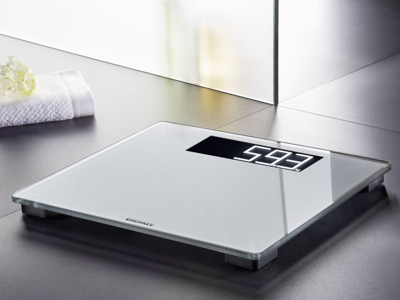 Digitale Waage auf einem Badezimmerboden zeigt das Gewicht 59,3 kg an.