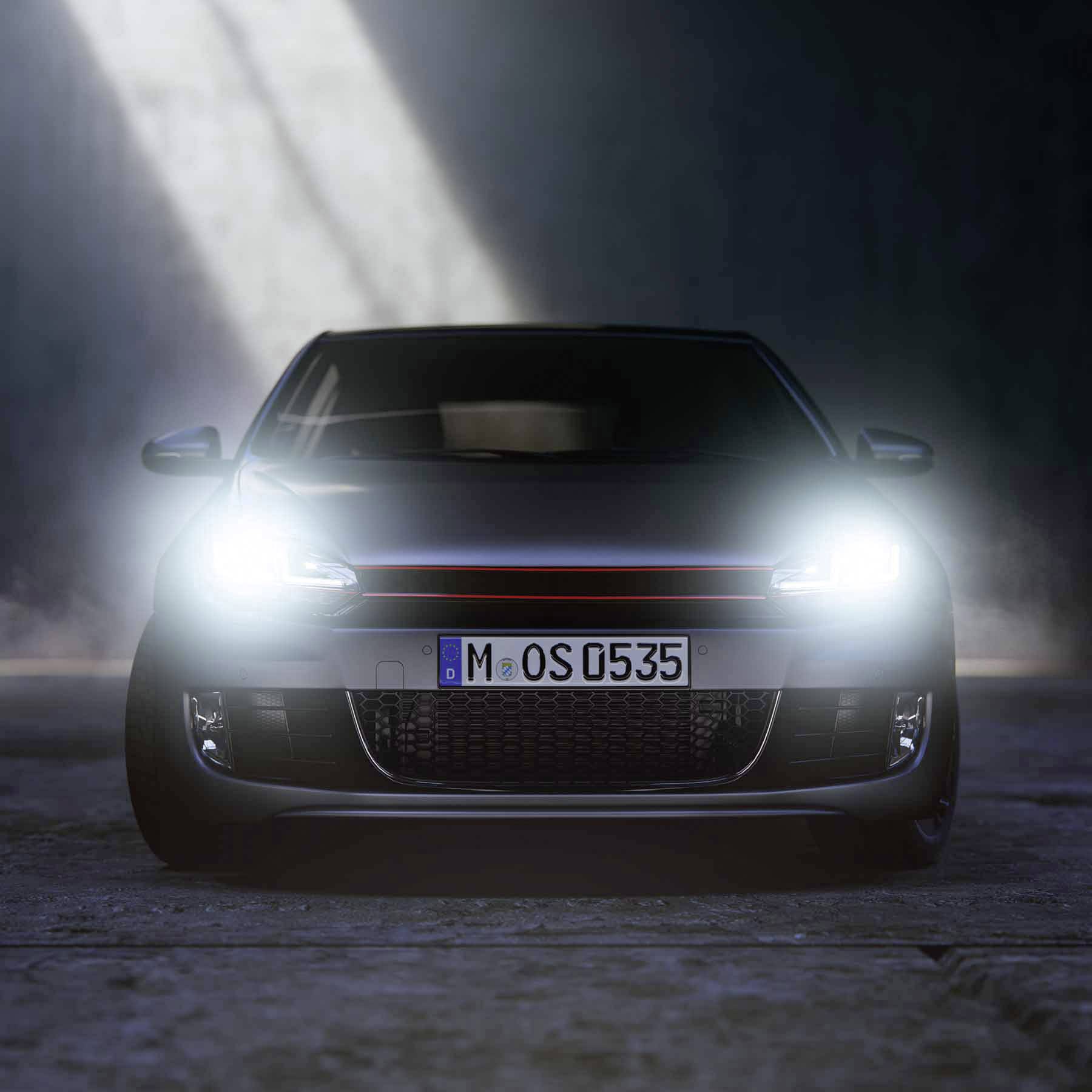 Ein Auto mit eingeschaltetem Frontlicht und sichtbarem Nummernschild steht in einer schattigen Umgebung mit Betonboden.