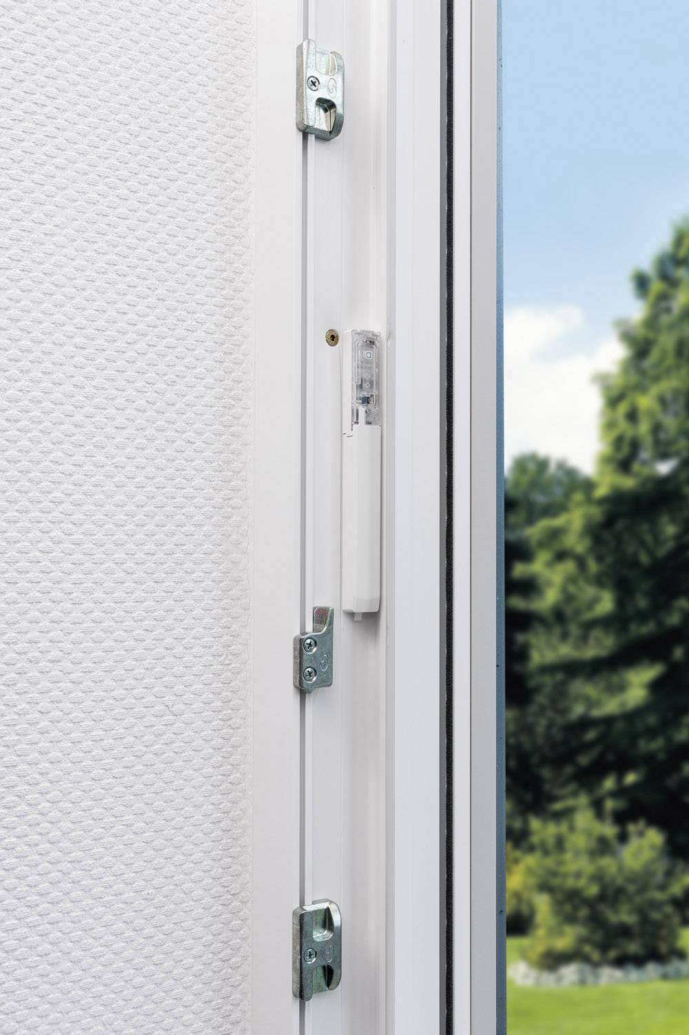 Nahaufnahme eines geöffneten Fensters mit Sicherheitsscharnieren. Durch das Fenster ist ein sonniger Garten mit Bäumen sichtbar.