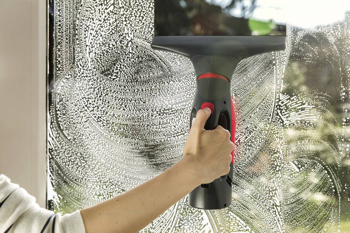 Eine Hand reinigt mit einem elektrischen Fensterreiniger ein Fenster. Die Scheibe ist teilweise mit Reinigungsflüssigkeit bedeckt.