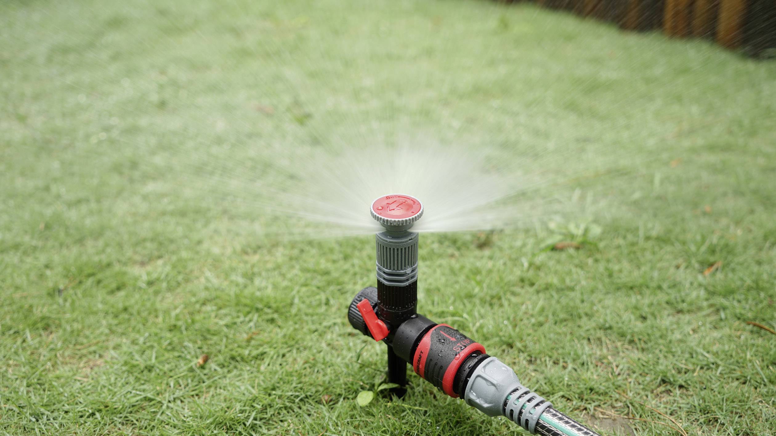Ein Rasensprenger auf grünem Gras verteilt Wasser gleichmäßig in einem kreisförmigen Muster.