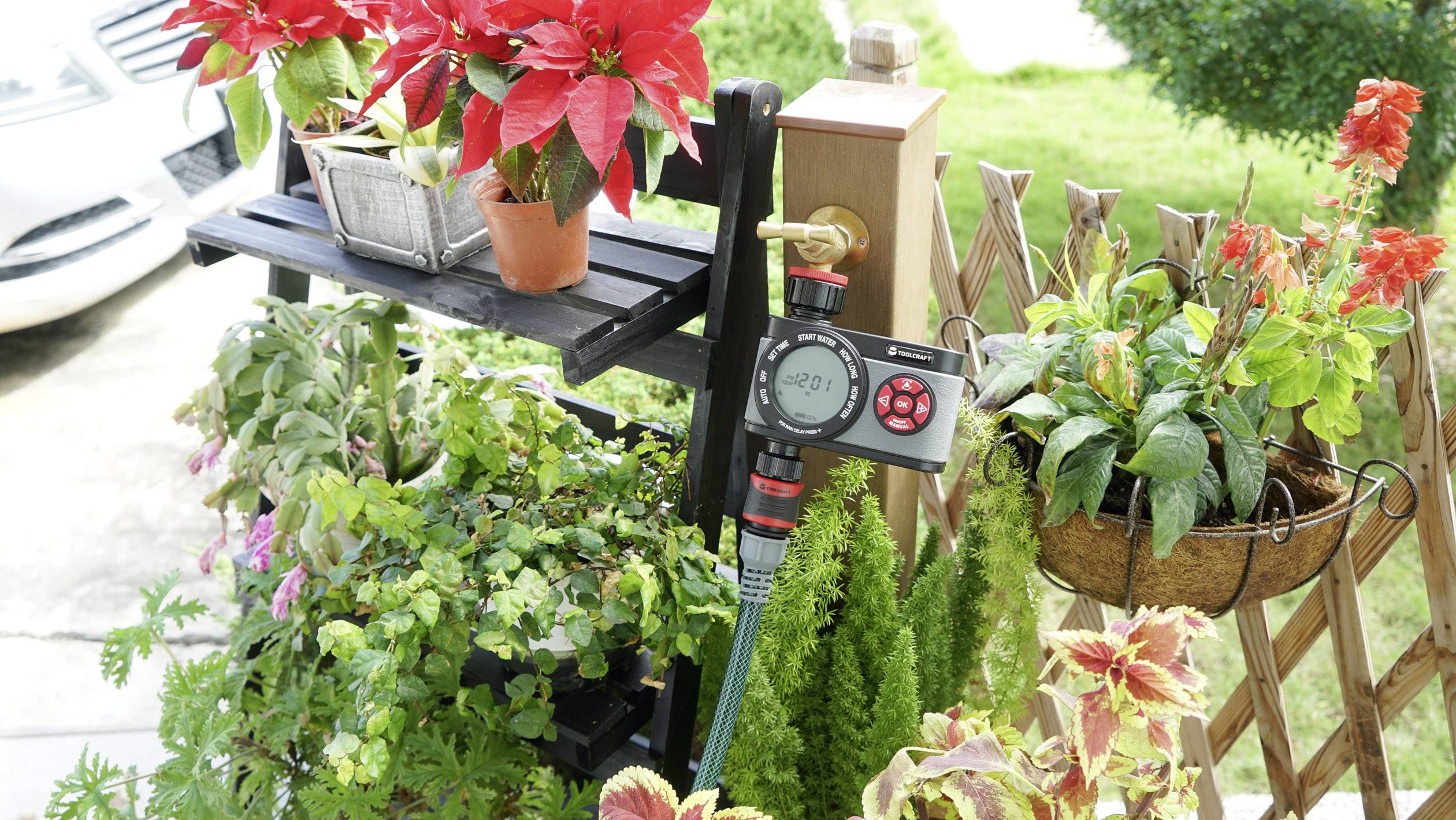 Gartenbewässerungssystem mit Zeitschaltuhr, umgeben von verschiedenen blühenden Pflanzen und grünen Blättern, im Freien installiert.