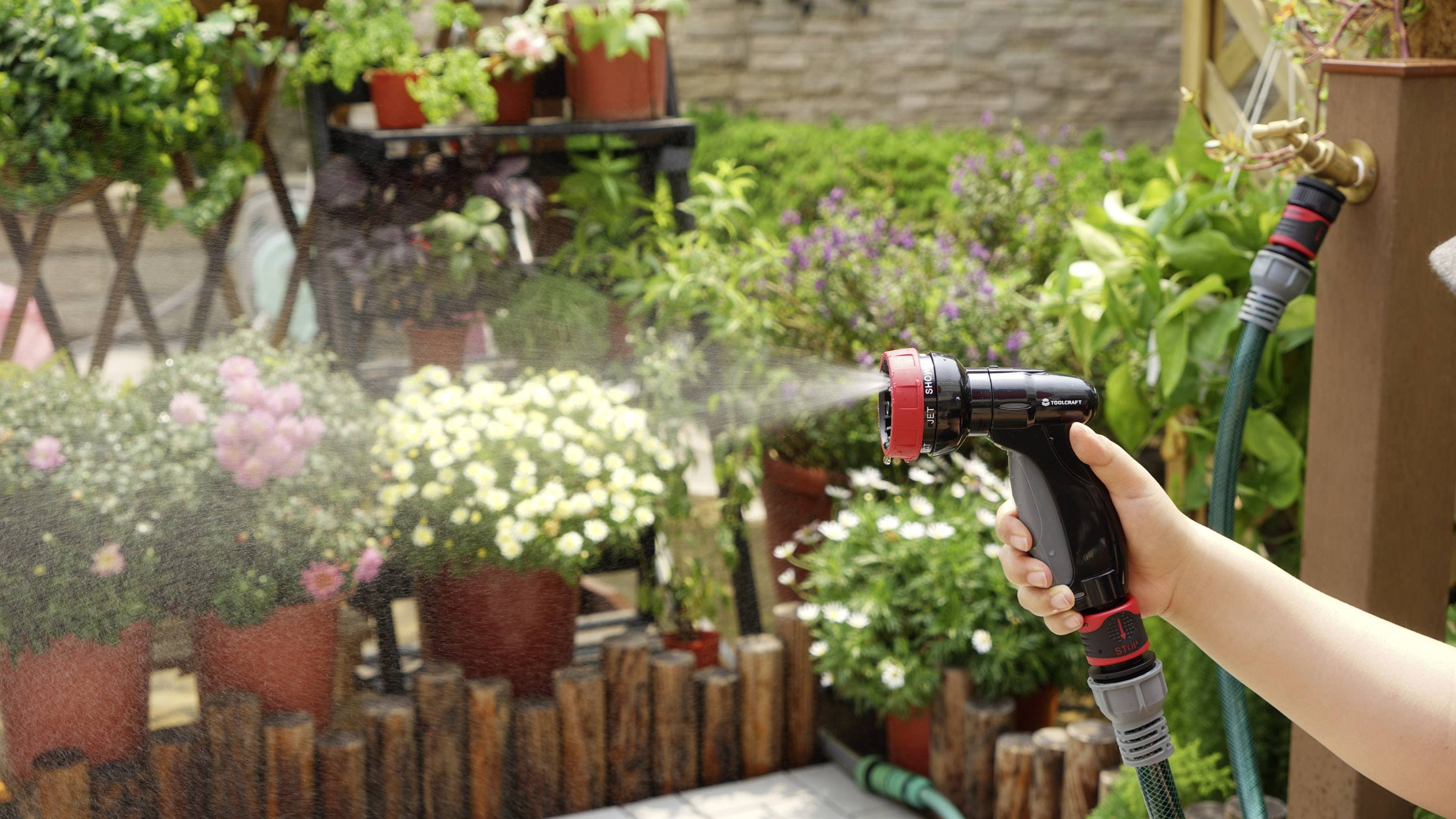 Eine Person gießt bunte Blumen in einem Garten mit einem Wasserschlauch, wodurch die Pflanzen bewässert werden.