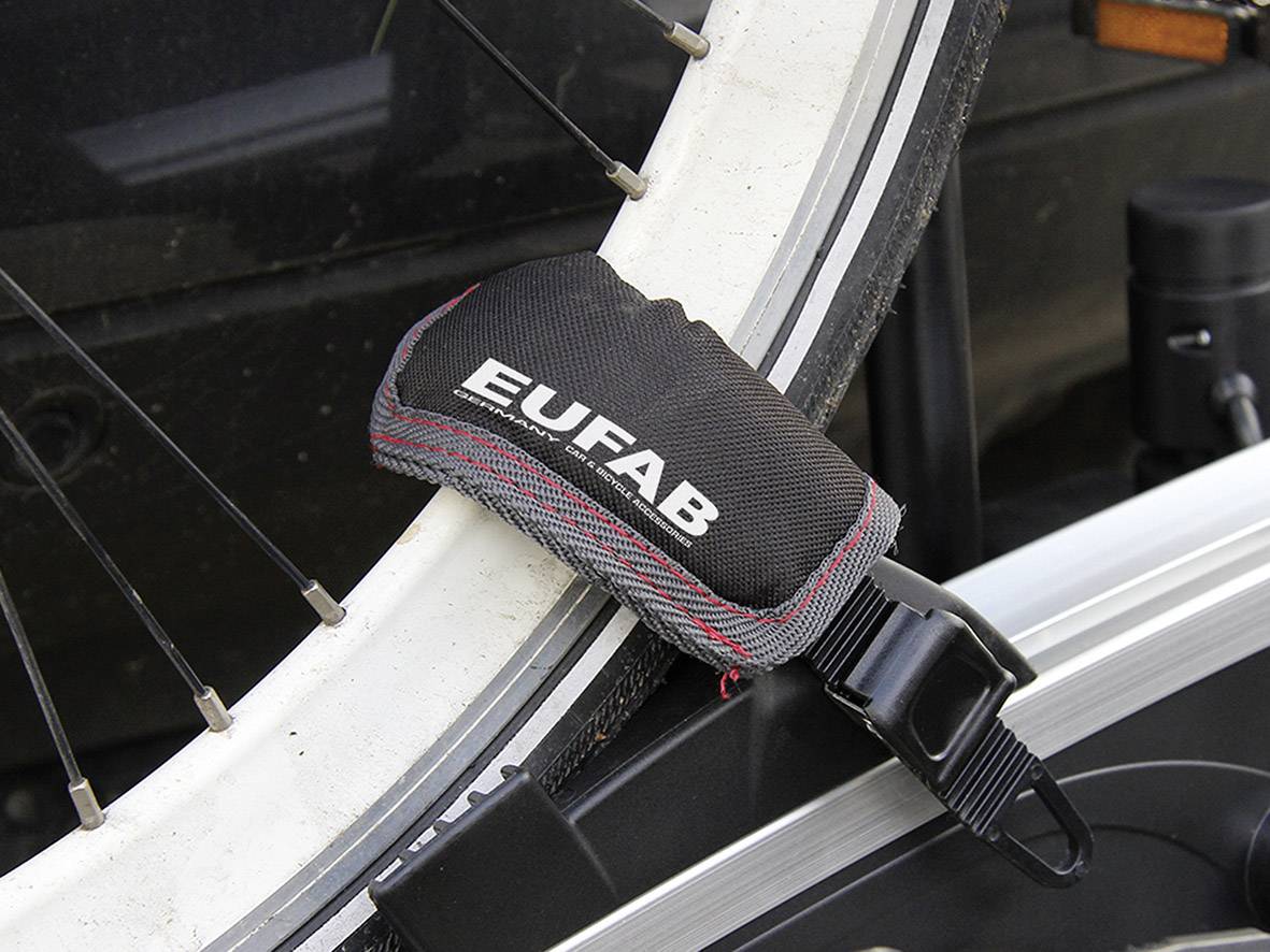 Ein Fahrradrad ist mit einem schwarzen Spannriemen mit der Aufschrift 'Eufab' gesichert, der an einem Fahrradträger befestigt ist.