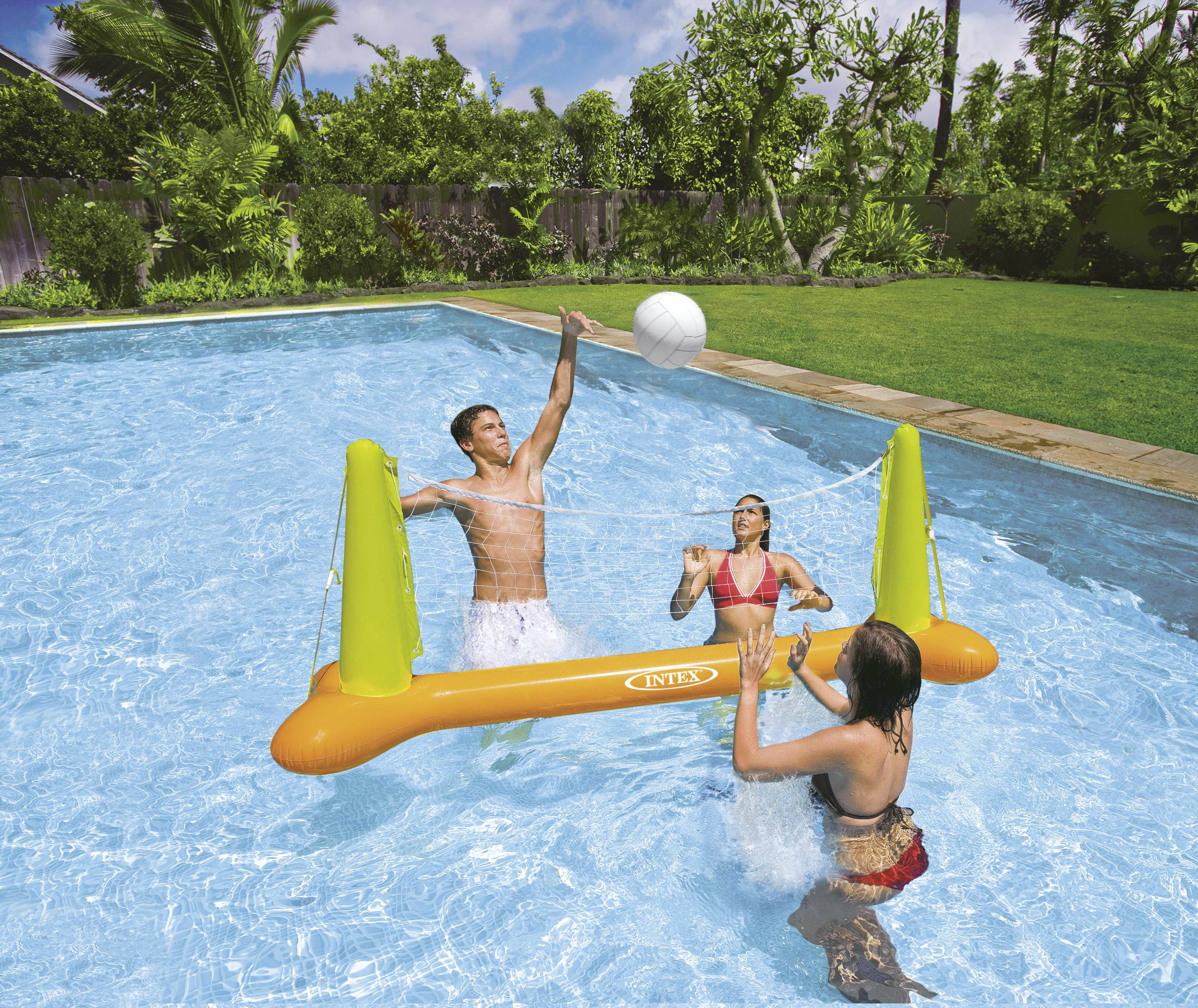 Drei Personen spielen Wasser-Volleyball in einem Pool, umgeben von grünen Bäumen. Ein Mann springt, um den Ball zu schlagen.