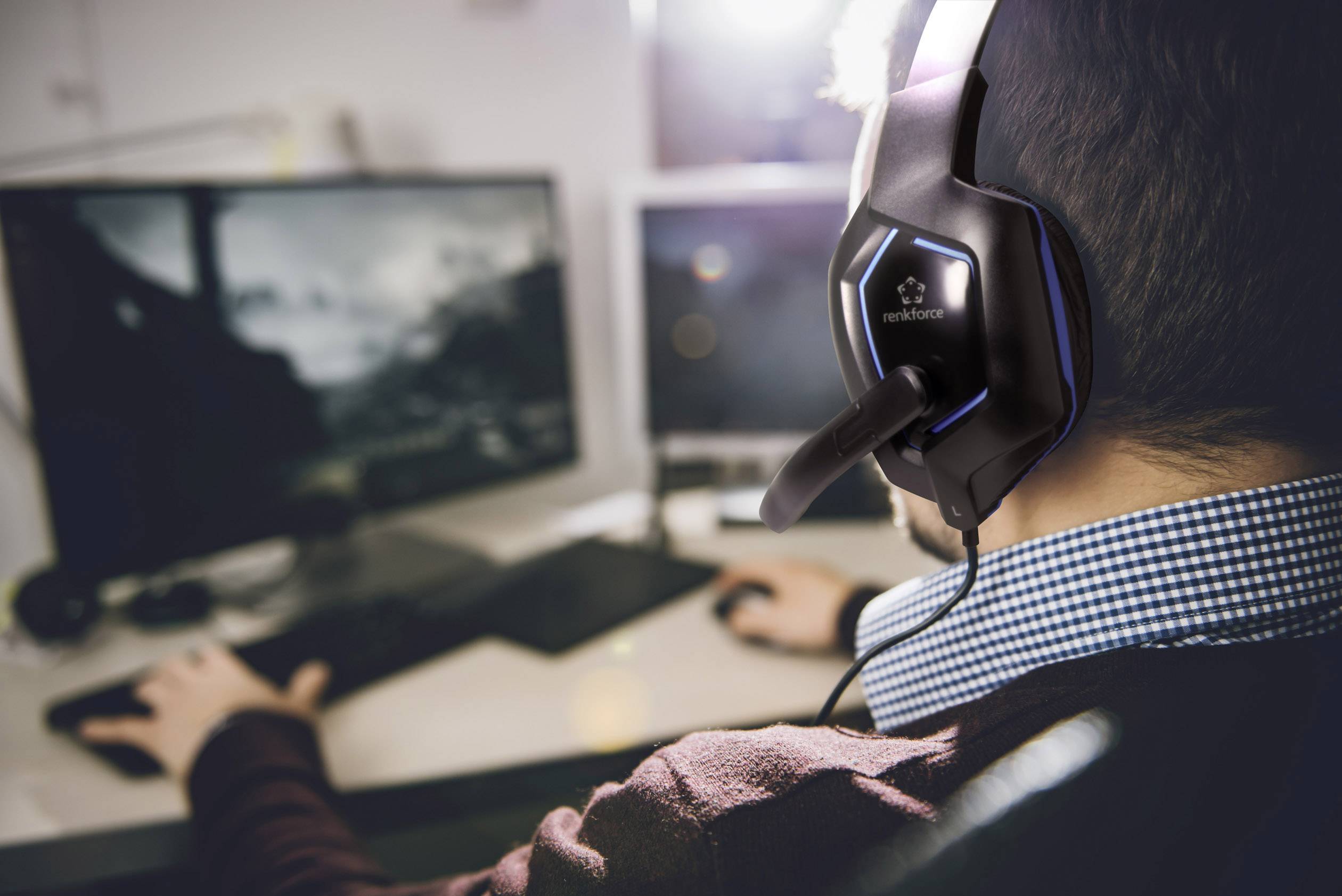 Person mit Headset vor zwei Computermonitoren sitzend, fokussiert auf Bildschirme, die verschwommen sind. Gaming- oder Arbeitsumgebung.
