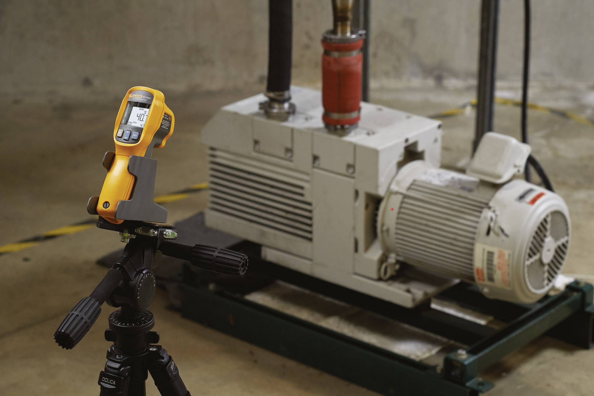 Ein Infrarotthermometer auf einem Stativ misst die Temperatur an einer Industriemaschine mit großem Motor in einer Fabrikumgebung.