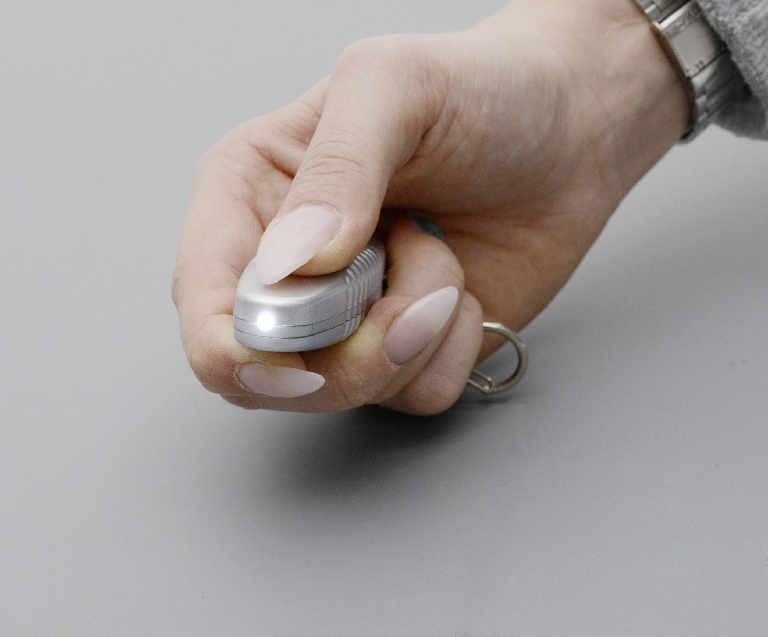 Eine Hand hält einen kleinen Taschenlampenschlüsselanhänger. Die Lampe leuchtet, während der Knopf gedrückt wird.