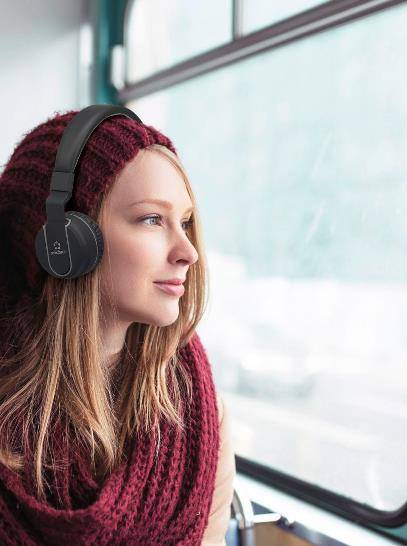 Eine Frau mit Kopfhörern sitzt in einem Bus und schaut aus dem Fenster. Sie trägt einen roten Schal und eine Mütze. Außenansicht verschwommen.