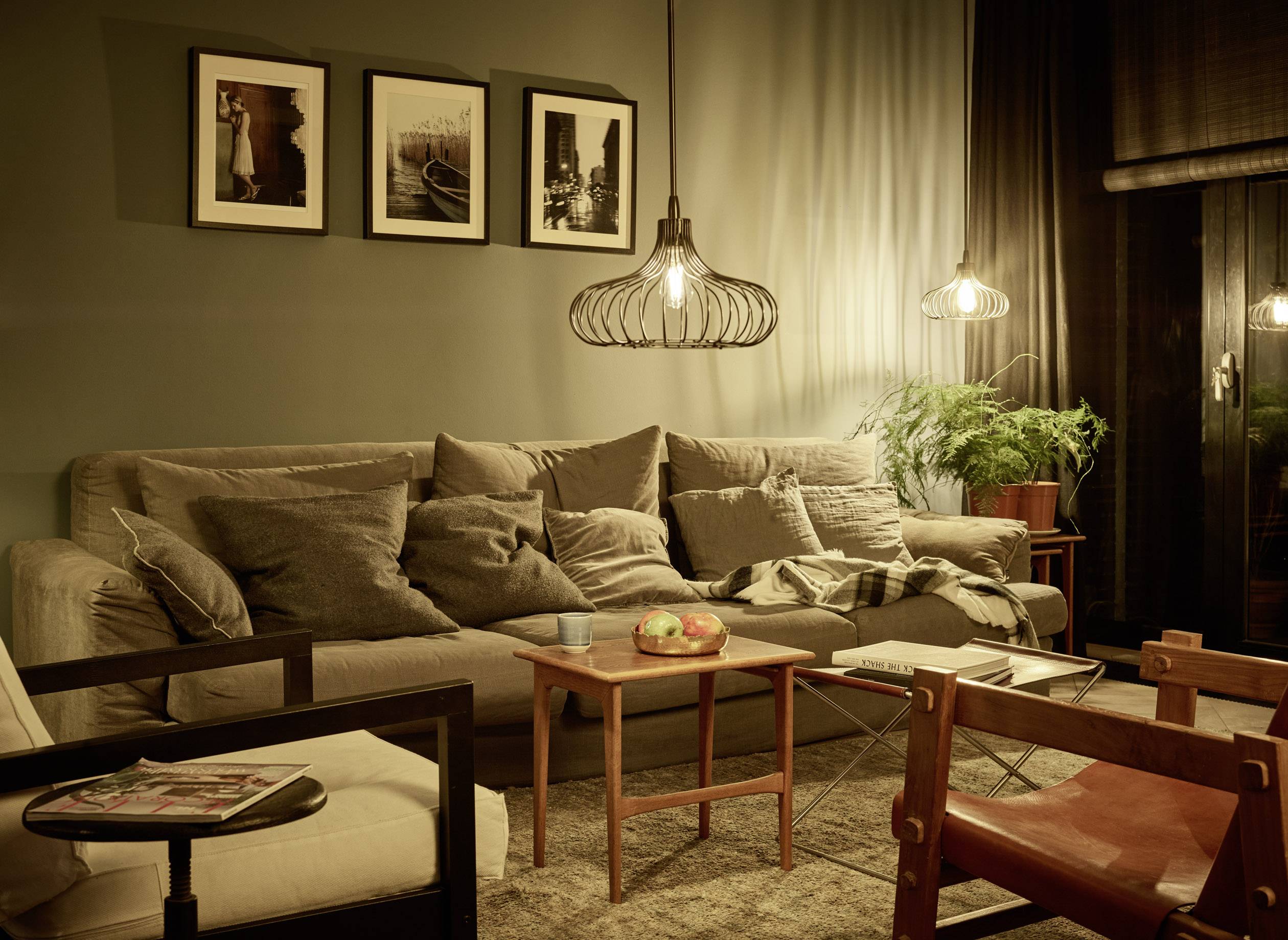 Gemütliches Wohnzimmer mit beige Sofa, dekorativen Kissen, hölzernem Couchtisch, Pendelleuchten und gerahmten Bildern an der Wand.