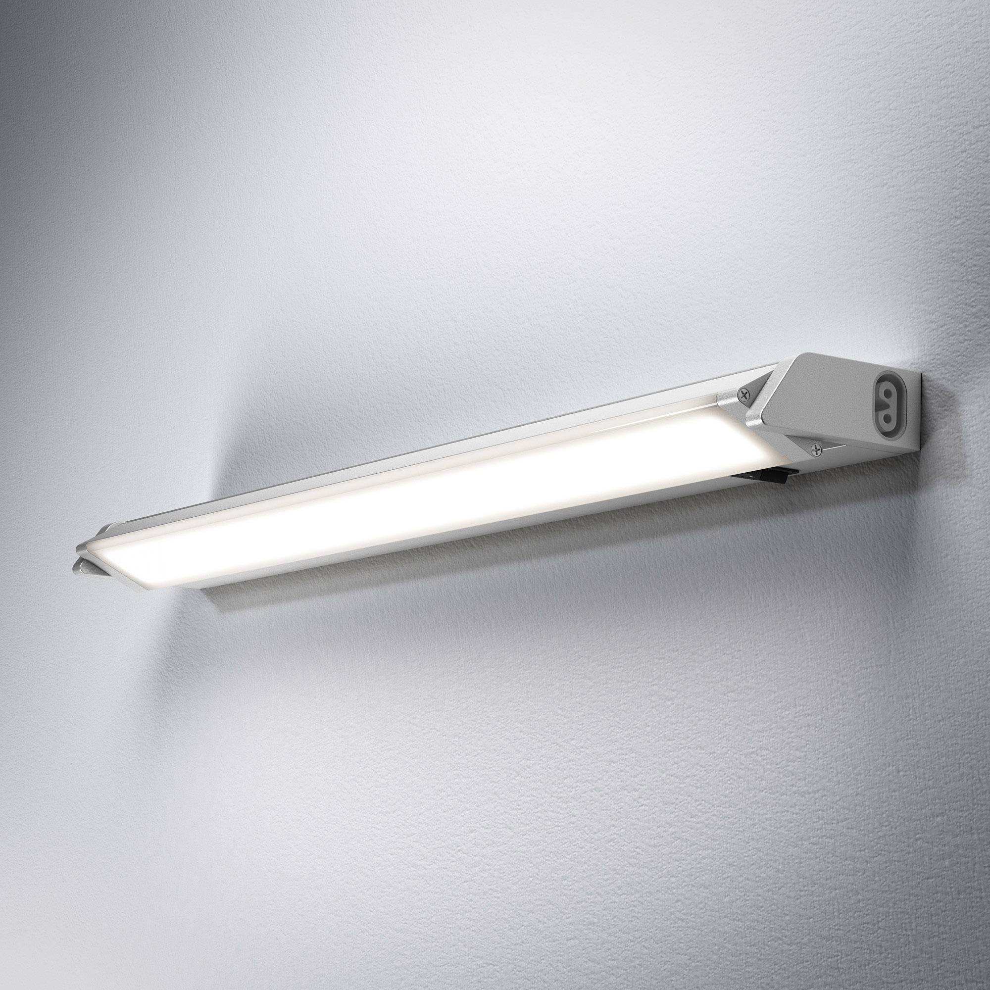 Leuchte an einer Wand montiert, strahlt weißes Licht aus. Modernes Design mit rechteckiger Form und silbernem Gehäuse.