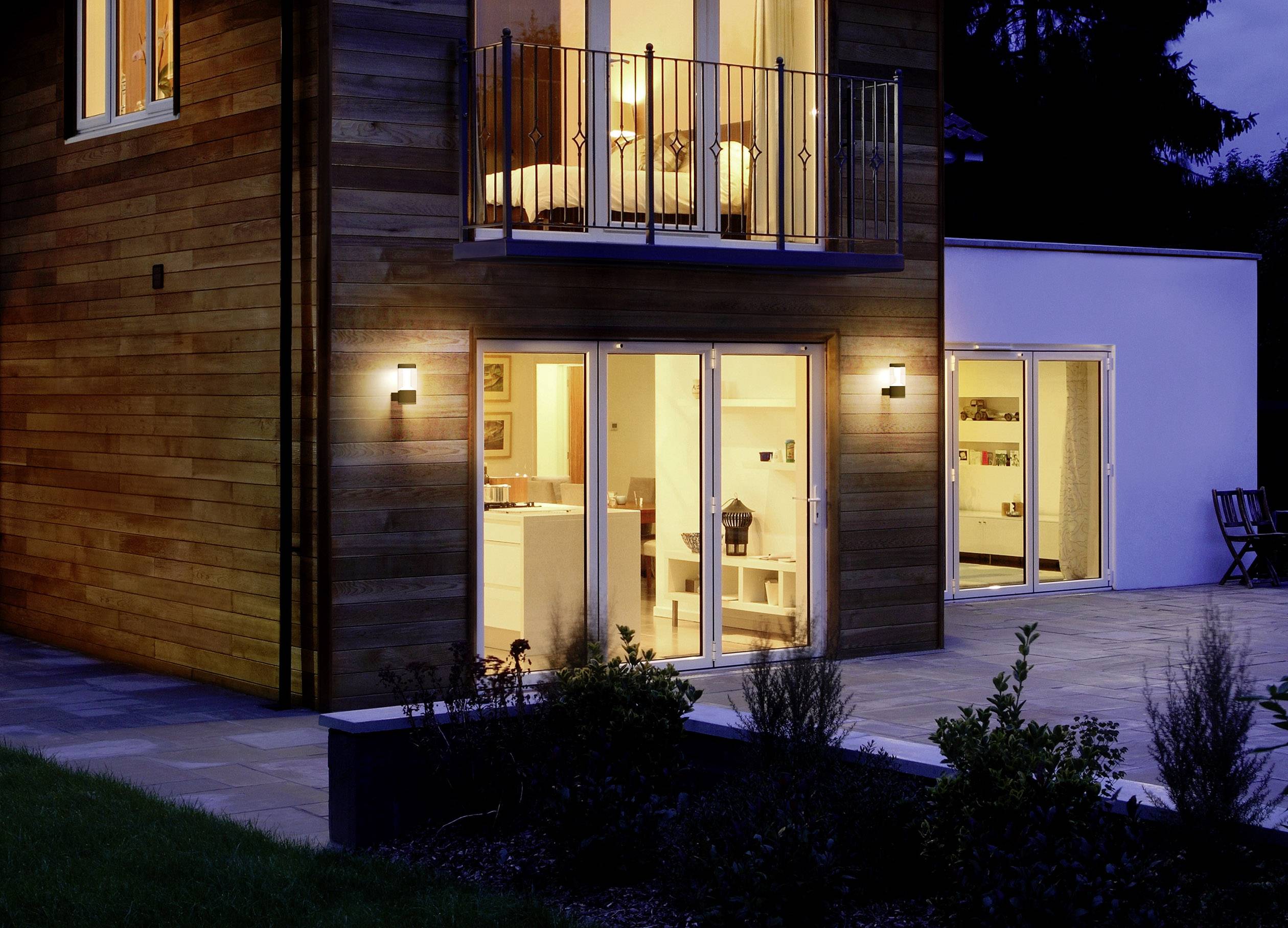 Modernes zweistöckiges Haus aus Holz und Beton, bei Nacht beleuchtet. Große Fenster geben den Blick auf stilvolle, helle Inneneinrichtung frei.
